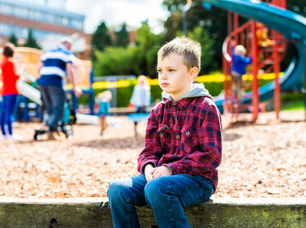 Photo of a child sat by themselves next to a playground